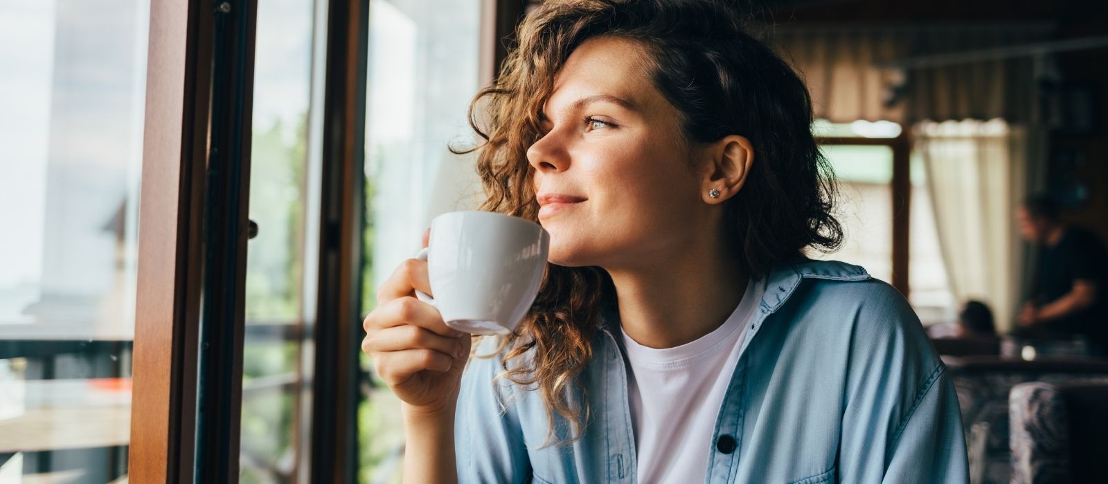 Woman with curly hair sipping coffee by a window
