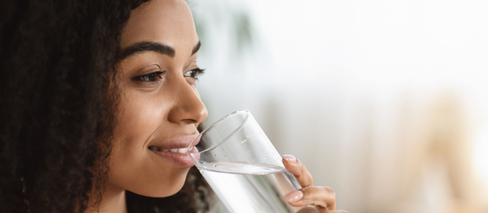 Woman with curly hair drinking a glass of water