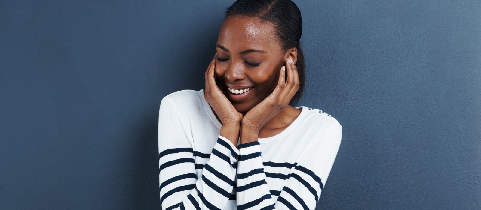 Smiling woman with her hands on her cheeks, eyes lowered