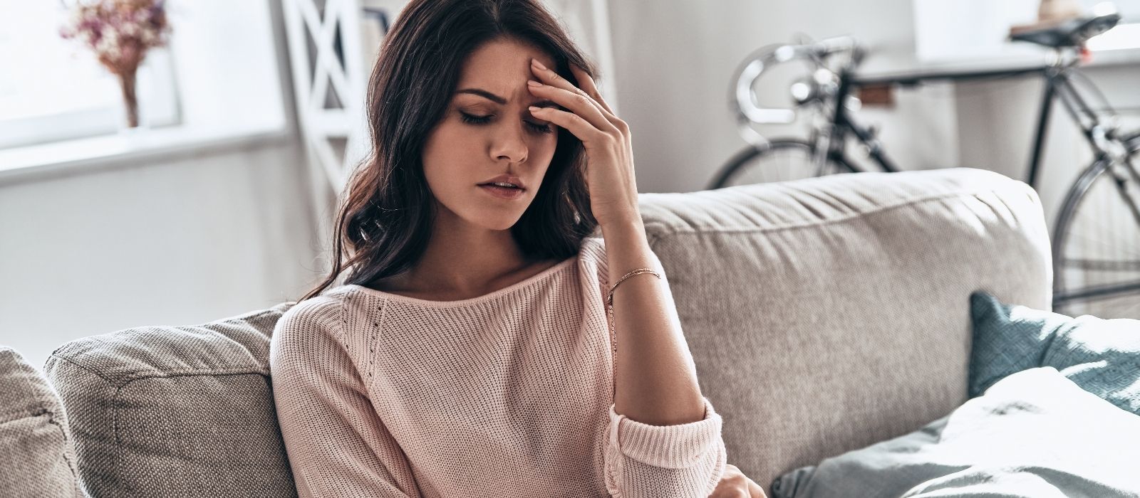Woman on a sofa holding her forehead, eyes closed