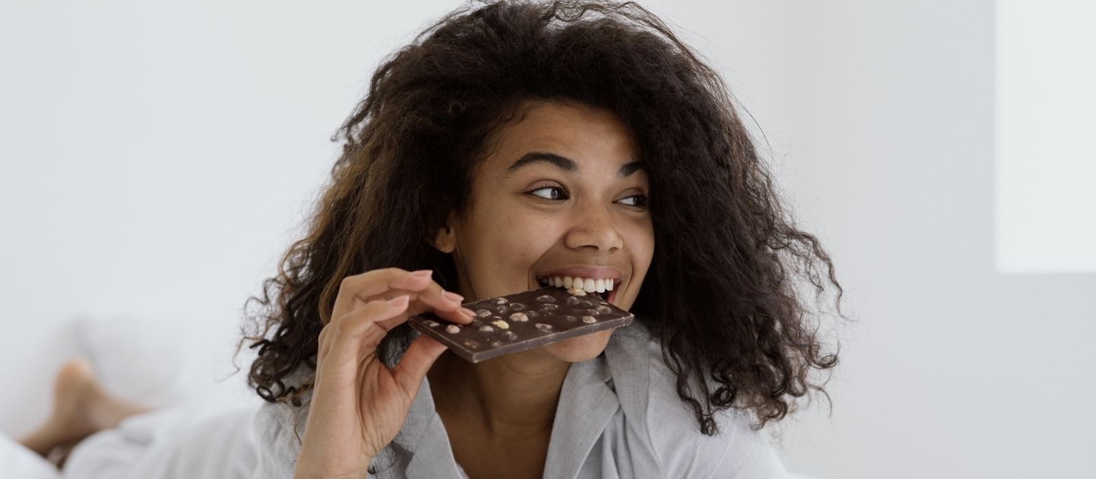 Smiling woman biting into a bar of nut chocolate