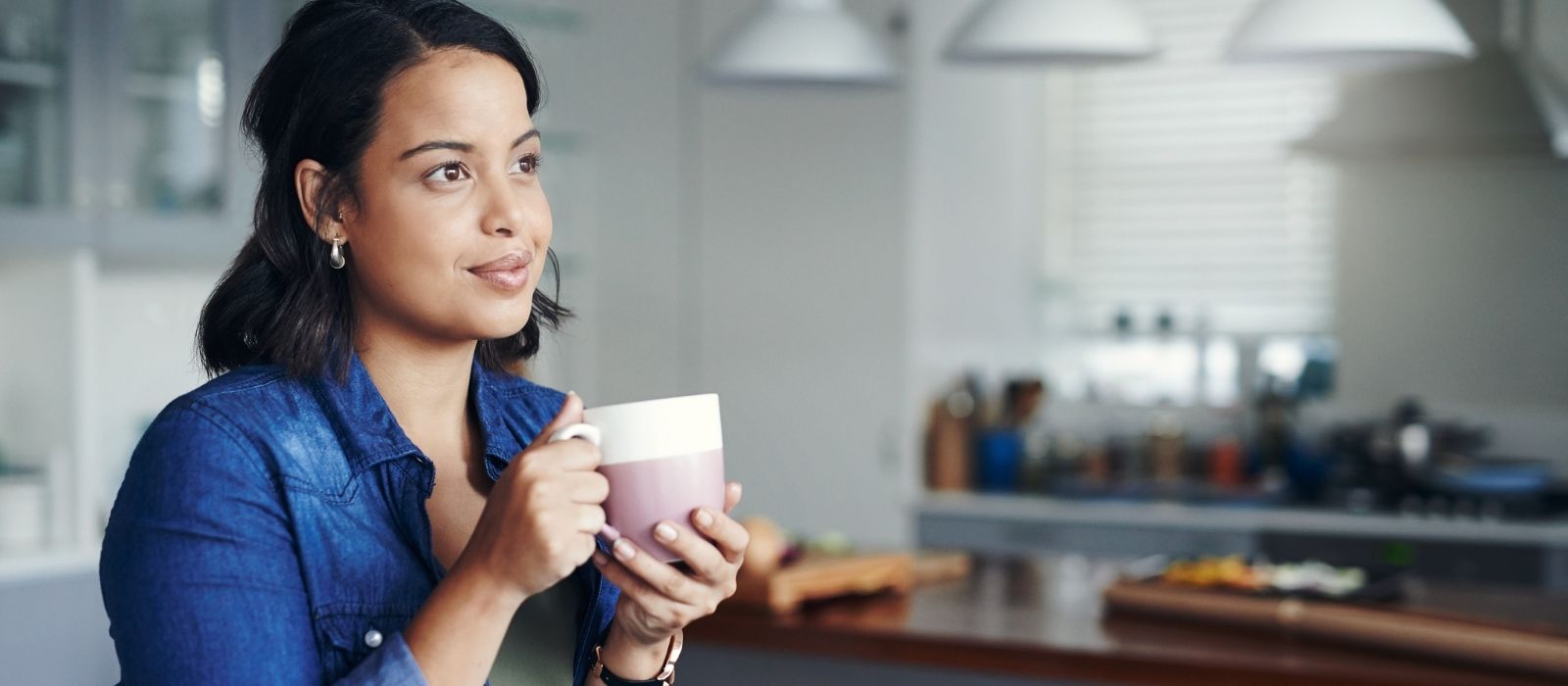 Woman holding a pink mug in a kitchen, looking away