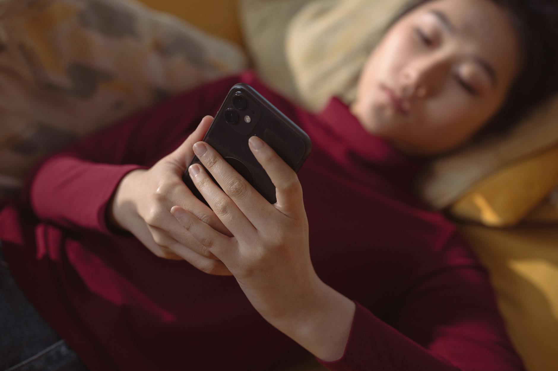 Woman sitting by window looking away from phone in morning light