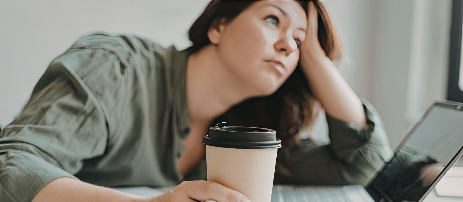 Tired woman at a desk with coffee and a laptop