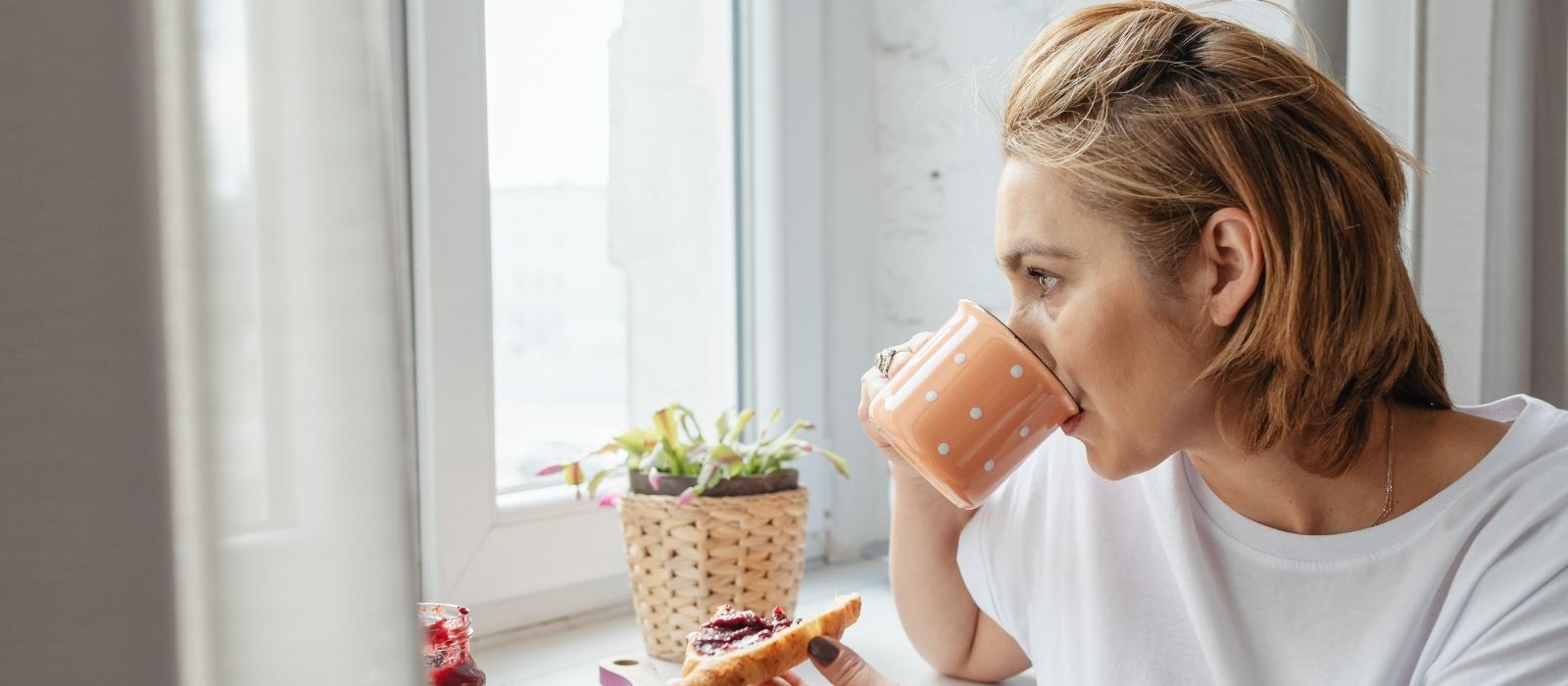 Woman drinking from a mug, looking out a window