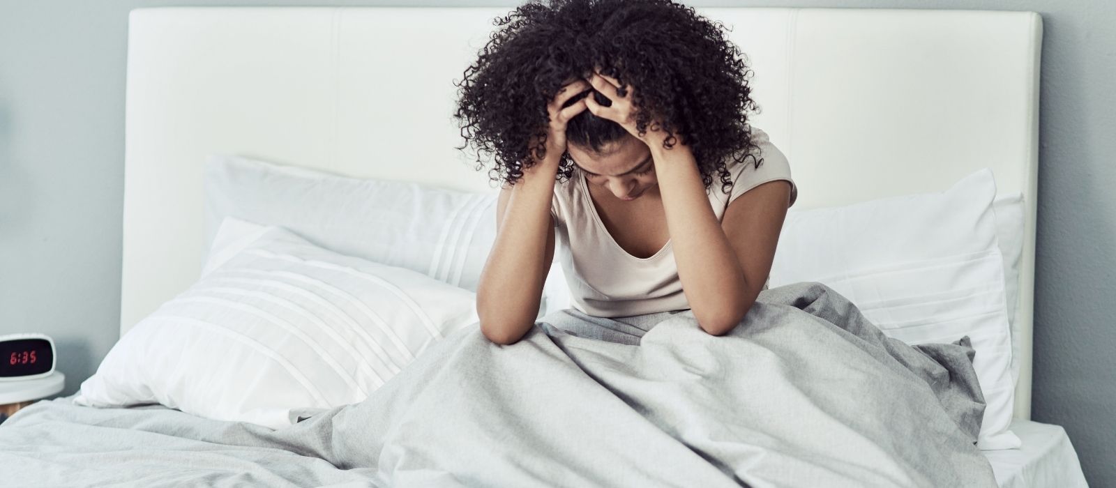 Woman sitting up in bed holding her head in her hands